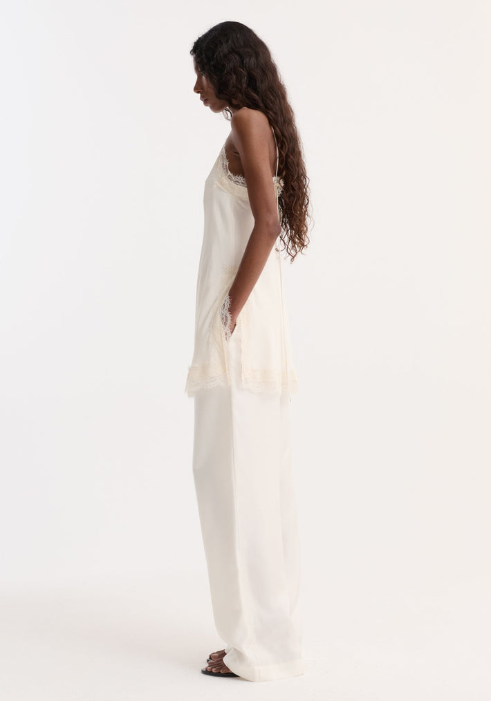 Lace camisole | off white: Side view of model in a cream lace-trimmed camisole with adjustable straps, paired with matching trousers and black slides.