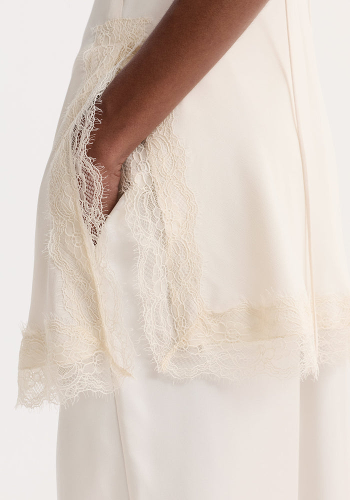 Close-up of a hand in a Lace camisole | off white, featuring silky fabric with floral lace trim, highlighting the elegance of the camisole's design.