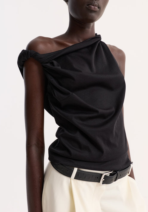 Person wearing a Sculptural cotton silk top | black, with a one-shoulder, twist detail, paired with high-waisted shorts and black flip-flops, standing relaxed.