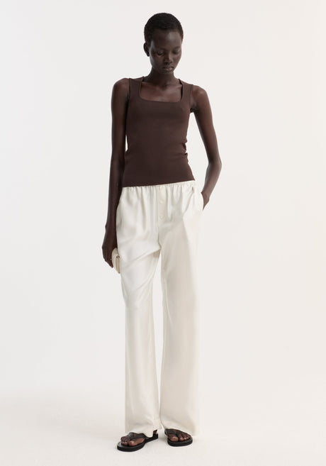 Model in a dark chocolate bustier-shaped knitted top, showcasing its fitted design, paired with high-waisted ivory trousers and black sandals.
