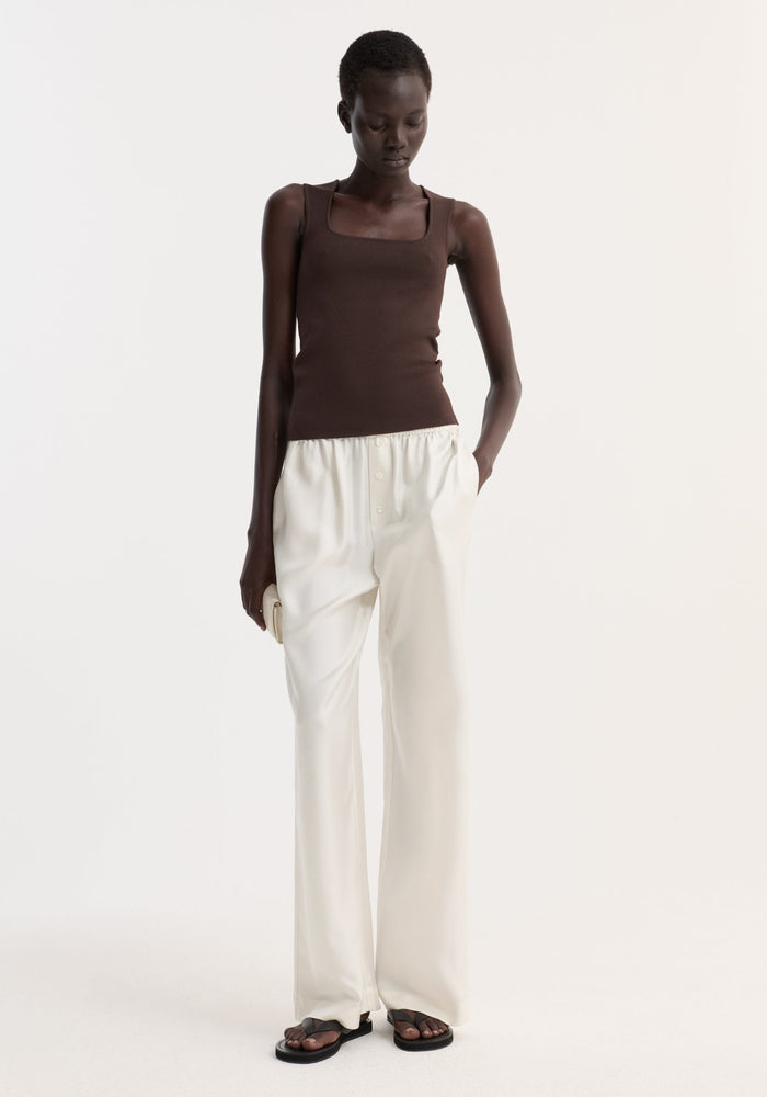 Model in a dark chocolate bustier-shaped knitted top, showcasing its fitted design, paired with high-waisted ivory trousers and black sandals.