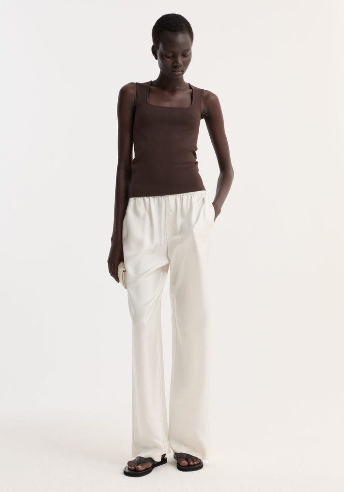 Model in a dark chocolate bustier-shaped knitted top, showcasing its fitted design, paired with high-waisted ivory trousers and black sandals.
