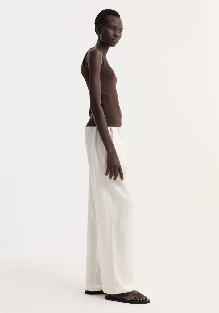 Tall person wearing Bustier shaped knitted top in dark chocolate, paired with high-waisted white trousers and black sandals, holding a neutral clutch.