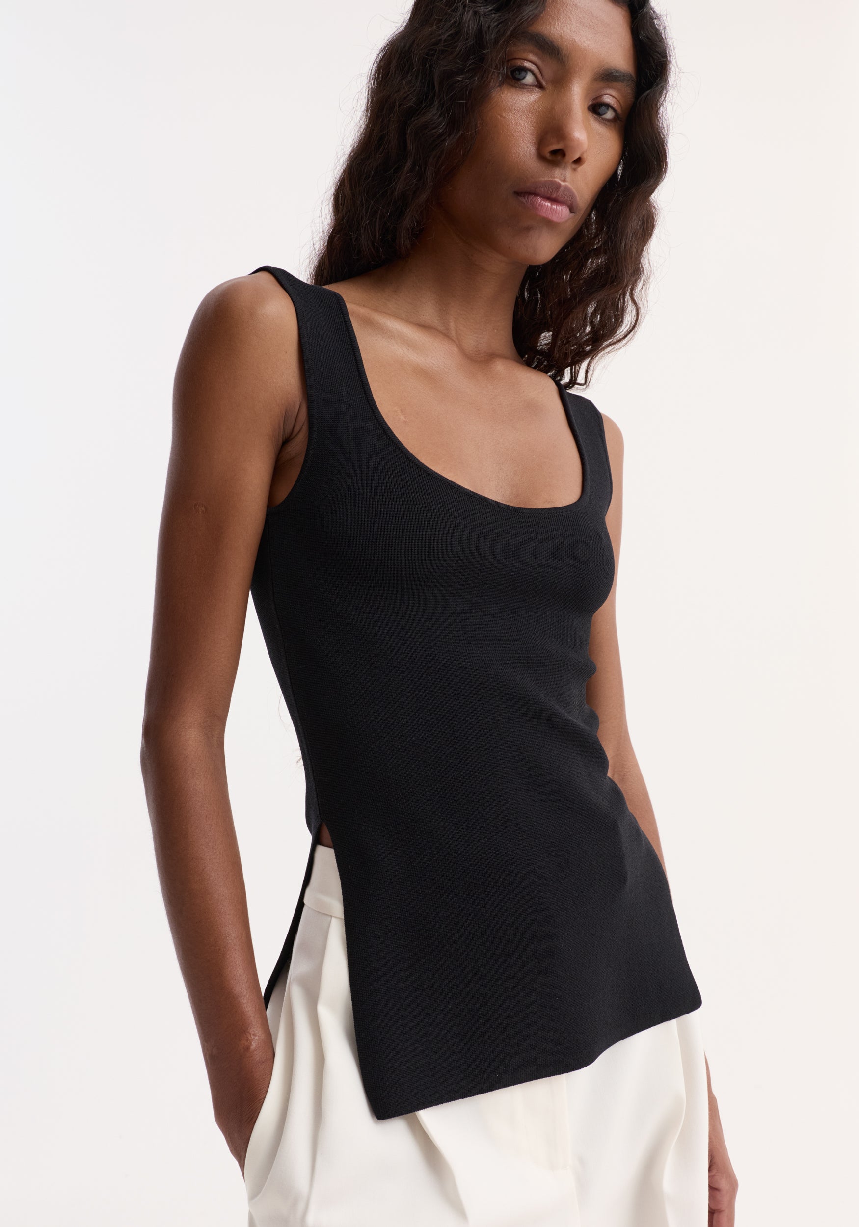Person wearing a Long knitted bustier top | black, featuring a scoop neckline and side slits, made from a viscose-blend yarn, emphasizing a fitted, elongated silhouette.