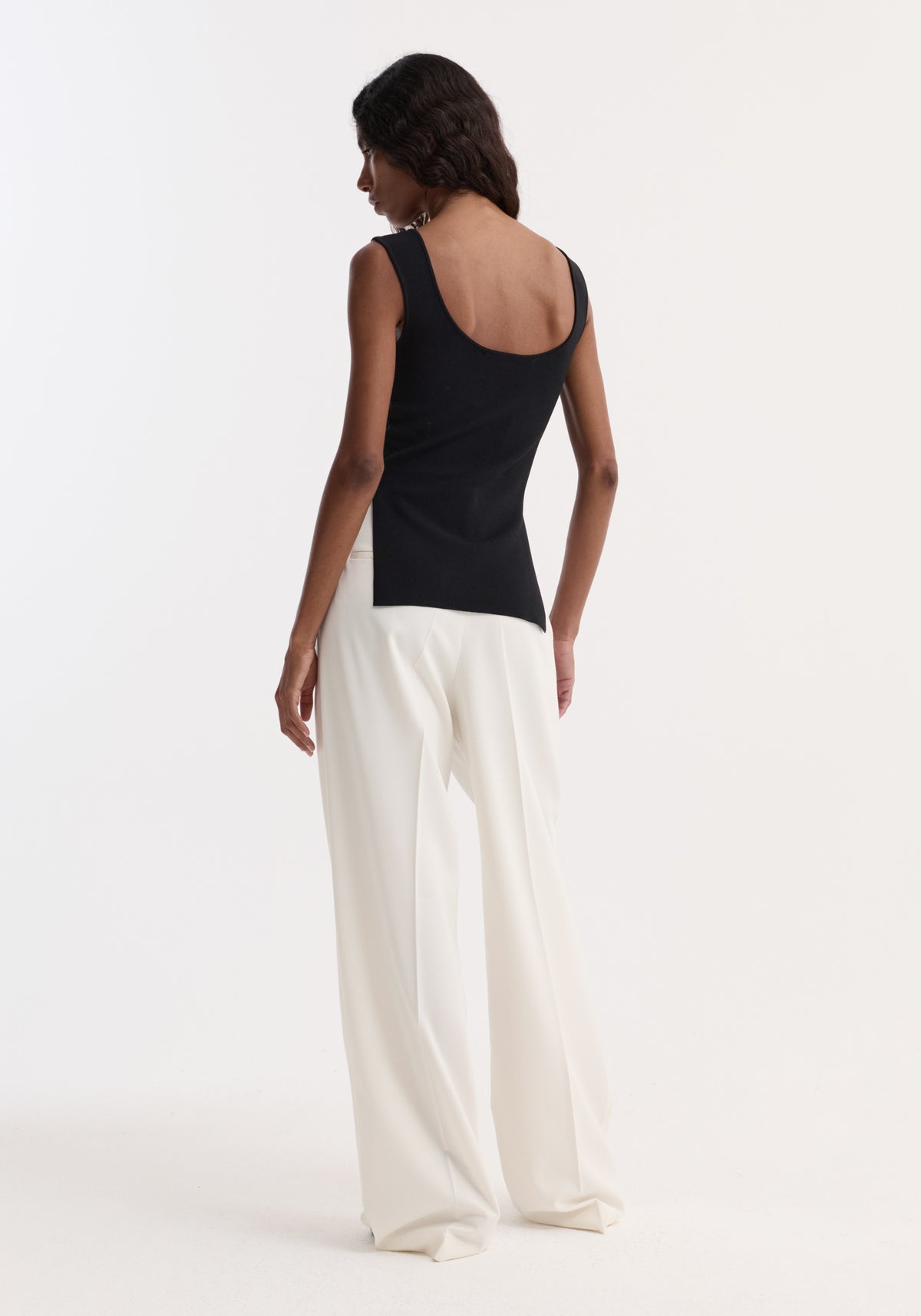 Model wearing Long knitted bustier top in black, featuring a scoop back and side slit, paired with high-waisted, wide-leg trousers.