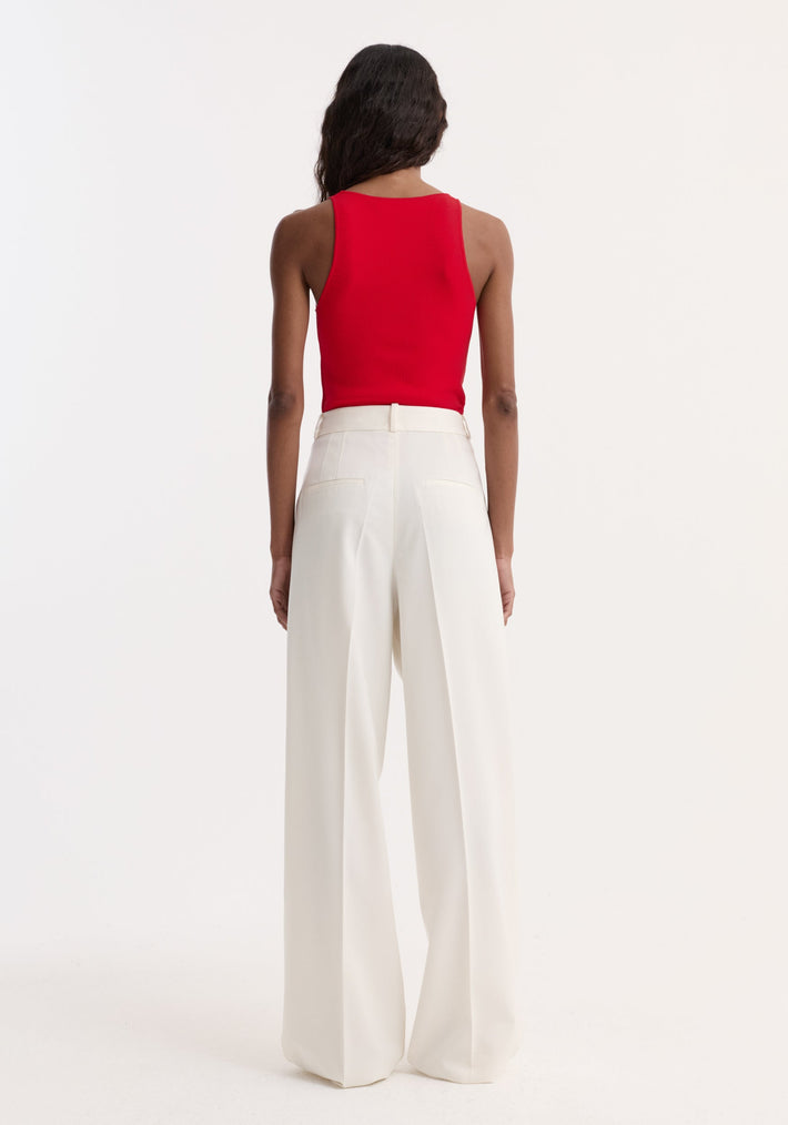 Rear view of a model in a red scoop neck knitted top, styled with high-waisted ivory-white wide-leg trousers. The top is fitted and sleeveless.