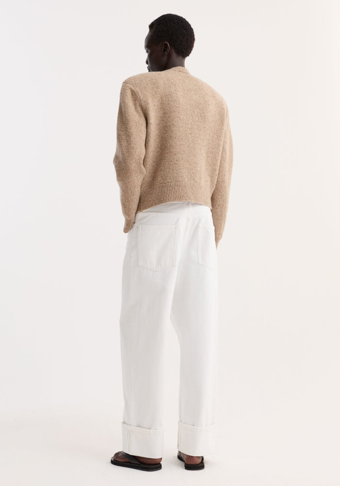 Person in Fine merino tweed cardigan | oat melange, cropped with shoulder pads, paired with high-waisted trousers and black sandals, showcasing minimalist style.