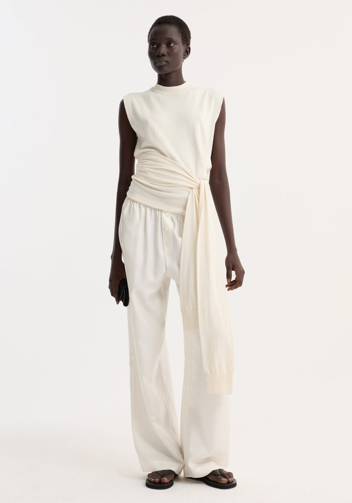 Model wearing an Open back knitted wrap top in off white, featuring a tied waist and open back, paired with wide-leg trousers and black sandals.