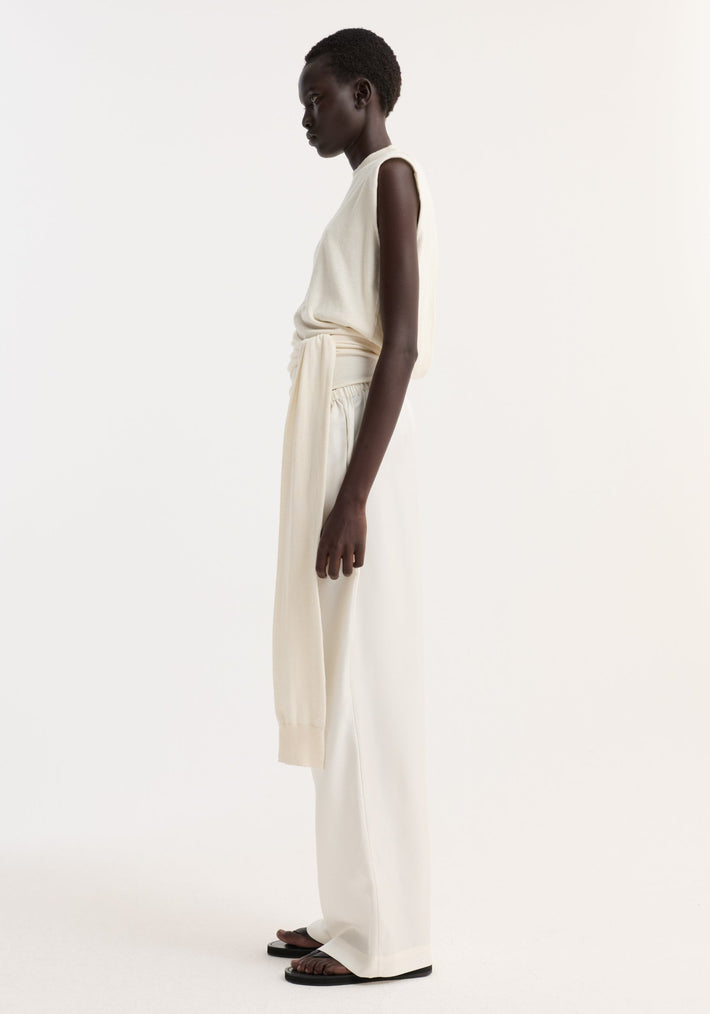 Dark-skinned model wears an Open back knitted wrap top | off white, featuring a knotted waist and sash-style sleeve extensions, paired with wide-leg trousers.