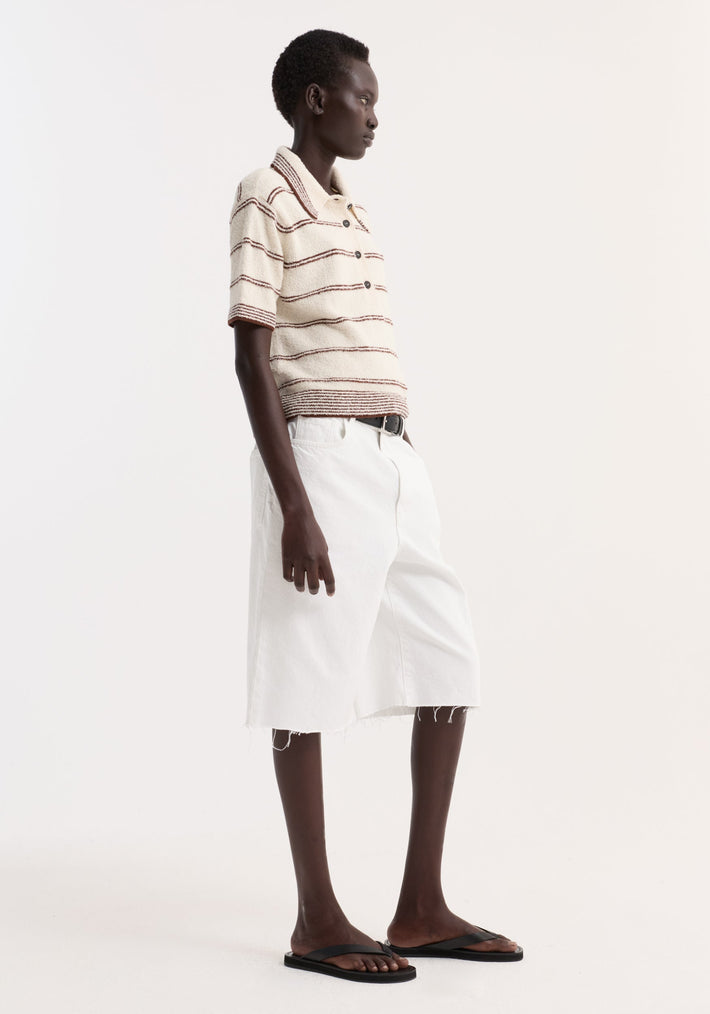 Model wears Towelling striped polo with cream/brown stripes, cropped fit, polo collar, four-button placket, paired with white raw-edge shorts and black flip-flops.