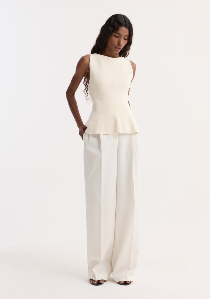 Sculptural knitted top | cream, features a sleeveless design with a peplum flare and boat neckline, paired with wide-leg trousers, worn by a model.
