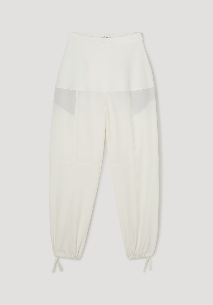 Sculptural trousers in off-white, featuring a wide waistband, semi-sheer hip panel, seam detailing, tapered legs with drawstring ties, and ankle adjusters for a ballooned silhouette.