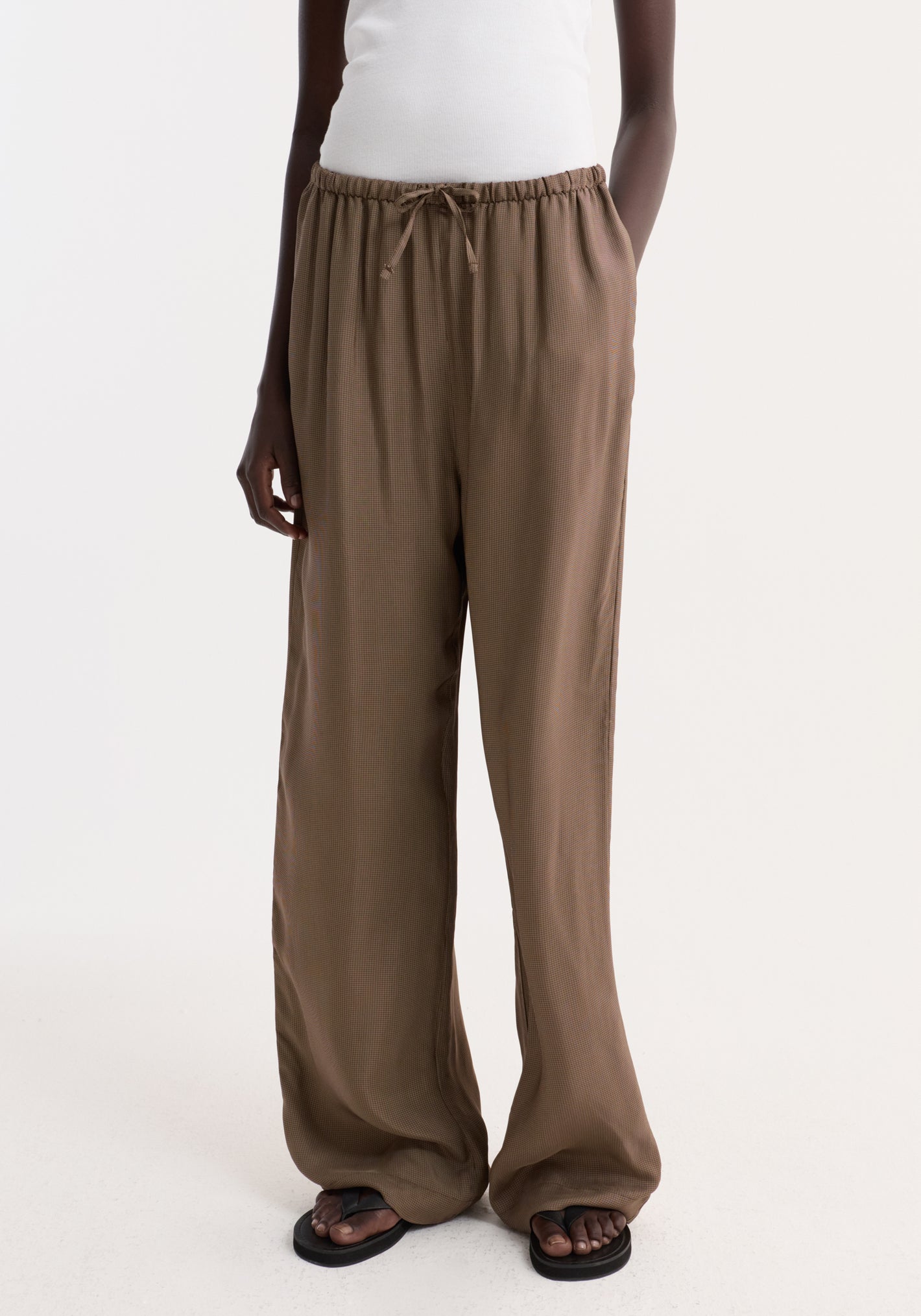 Person wearing Relaxed fit trousers | brown mini check with wide legs and a drawstring waistband, styled with side pockets and black flip-flop sandals.