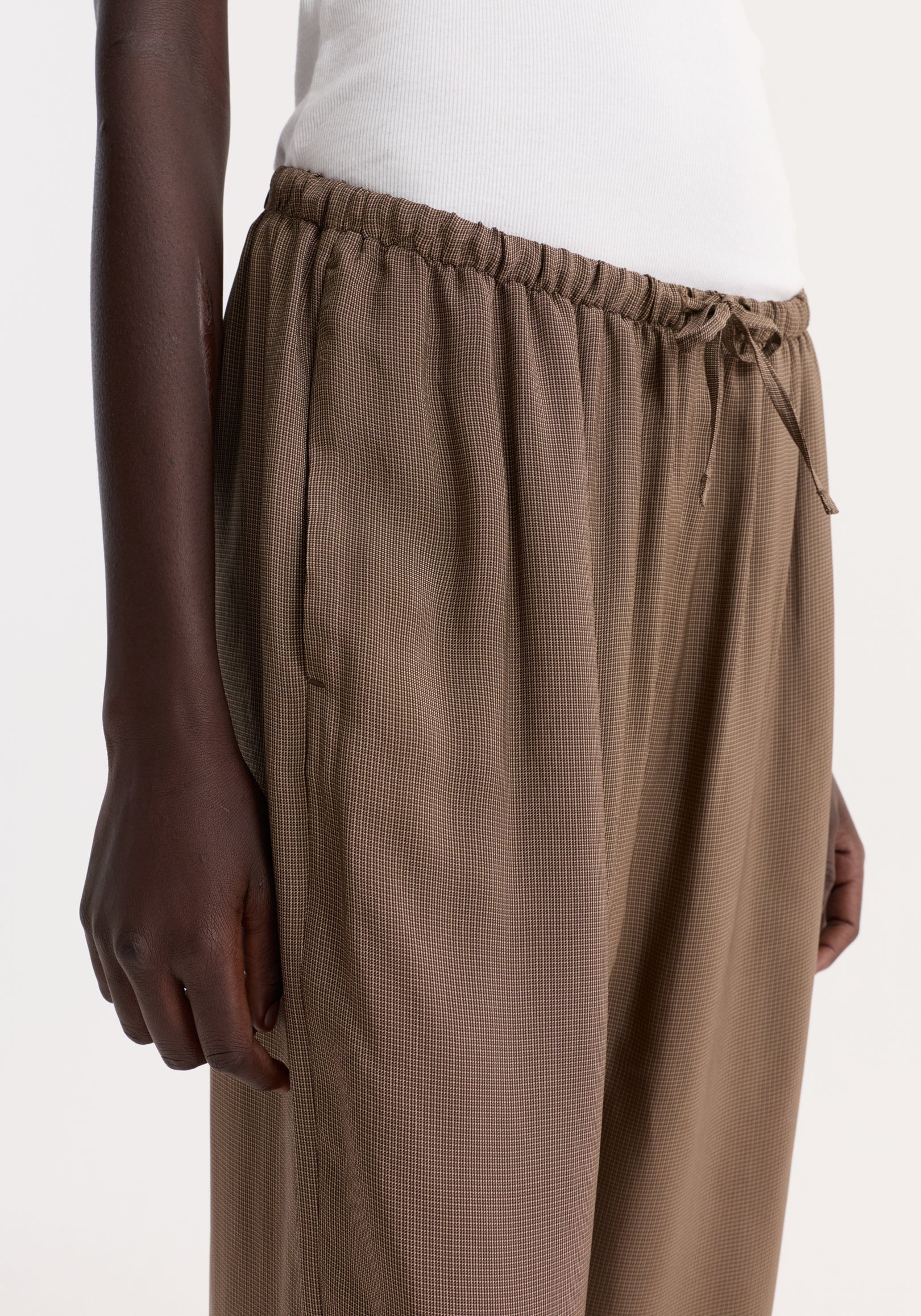 Person wearing relaxed fit trousers with a mini check pattern, featuring a drawstring waistband and wide legs, showcasing a reimagined classic pyjama style.
