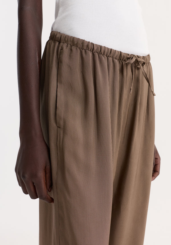 Person wearing relaxed fit trousers with a mini check pattern, featuring a drawstring waistband and wide legs, showcasing a reimagined classic pyjama style.