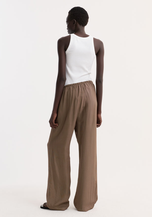 A person wears relaxed fit trousers with a wide leg and drawstring waistband. The trousers feature a brown mini check pattern and side seam pockets.
