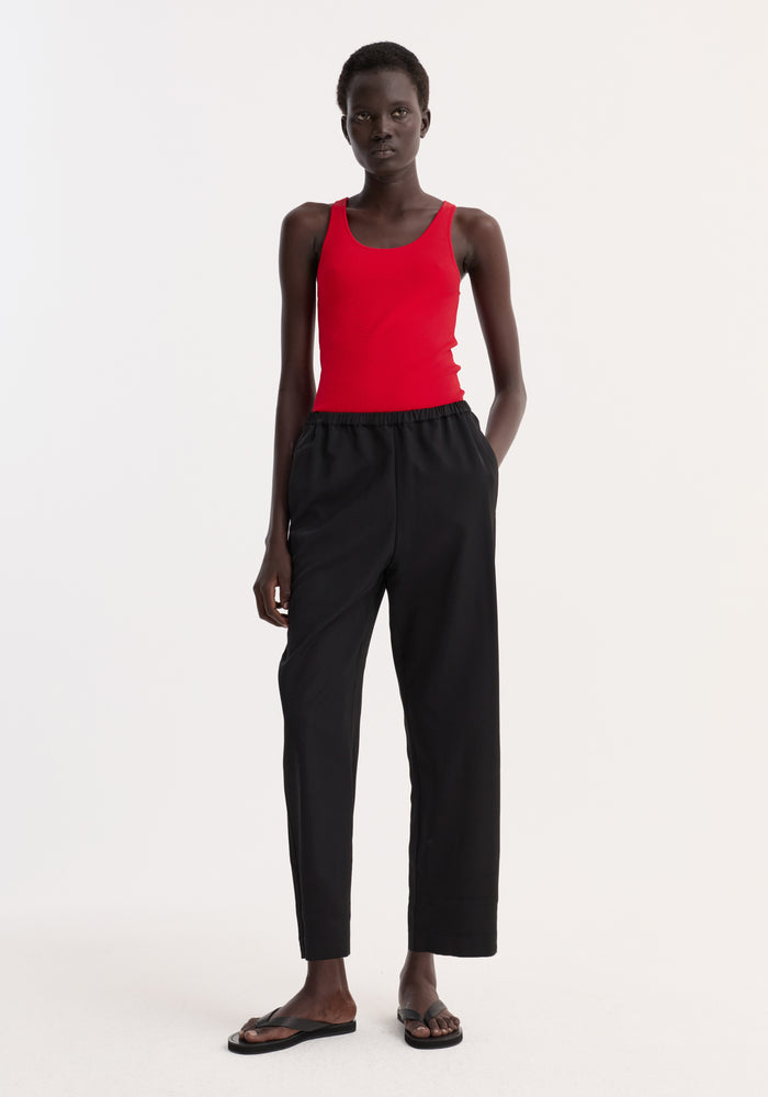 Cropped wide leg trousers in black with an elasticated waist and side pockets, shown on a tall model wearing a bright red tank top.