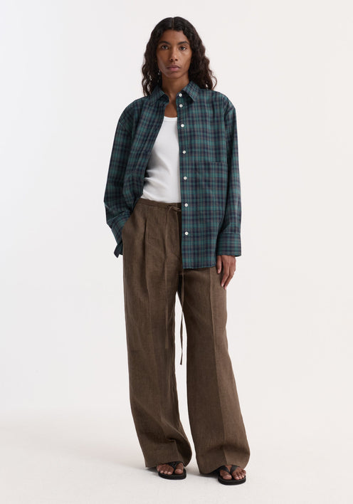 Woman wearing Relaxed drawstring trousers in brown melange with a wide leg and drawstring waistband, styled with a plaid shirt and sandals.