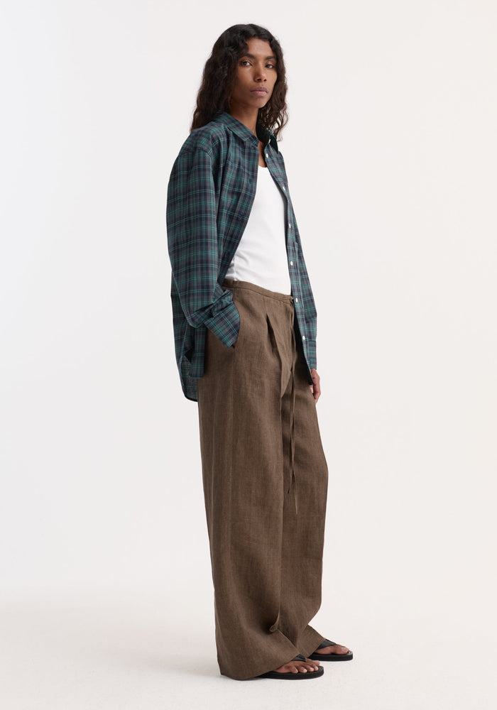 Model wearing Relaxed drawstring trousers | brown melange with a wide-leg fit, paired with a plaid shirt and white tank, showcasing a comfortable, minimalist style.
