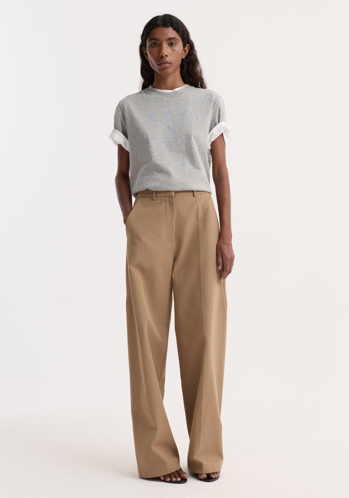 Woman wearing a gray short-sleeve t-shirt and beige Classic loose fit chino | beige pants with hands in pockets, standing against a plain light background.