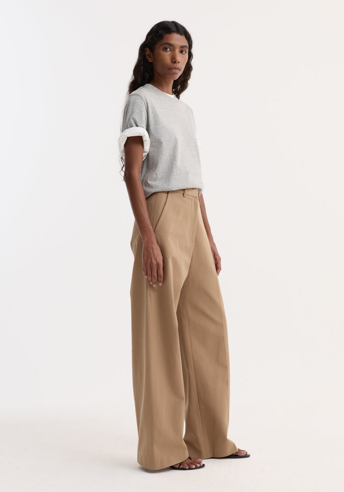 Woman in minimalist outfit wearing Classic baggy chino trousers, featuring high-waisted, wide-leg design paired with a light grey T-shirt and black sandals.