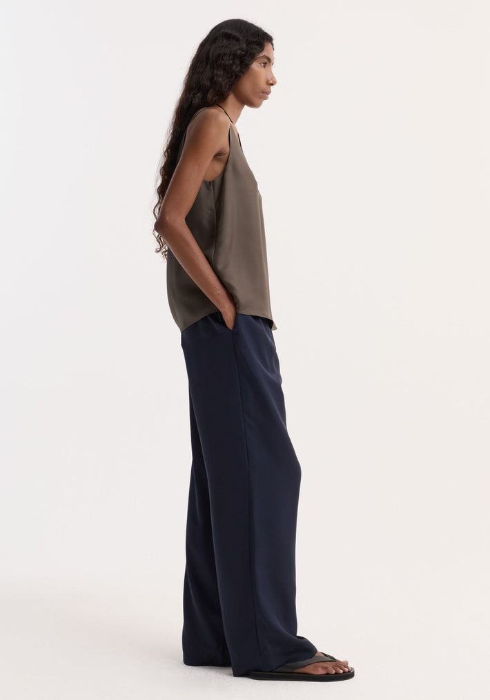 Silk pyjama trousers | night shown on a model with wide-leg design, elastic waistband, faux fly, and two-button detail, styled with an olive tank top.