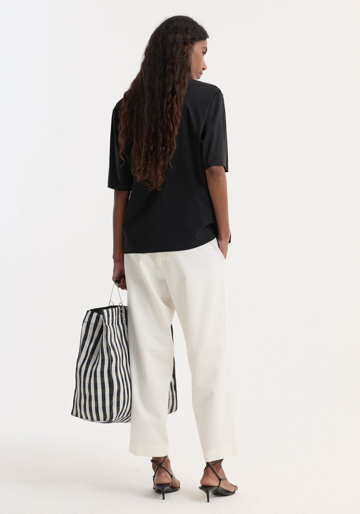 Woman wearing cropped wide leg trousers with an elasticated waist and side pockets, paired with black sandals and holding a striped tote bag.