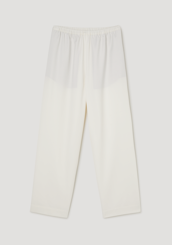 Cropped wide leg trousers in off-white, featuring an elastic waistband, ankle-length fit, and side seam pockets, laid flat against a neutral background.