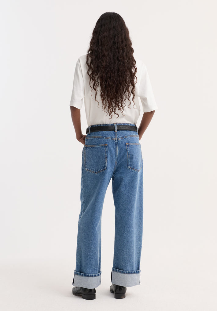 Turn-up baggy denim in heritage blue, featuring a low-rise, wide-leg fit, rolled cuffs, and a black belt, worn by a model with wavy hair.