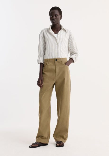 Model wearing Baggy fit denim | sage, featuring high-waisted olive-green wide-leg trousers with a low-waist baggy fit, paired with a striped shirt and flip-flops.