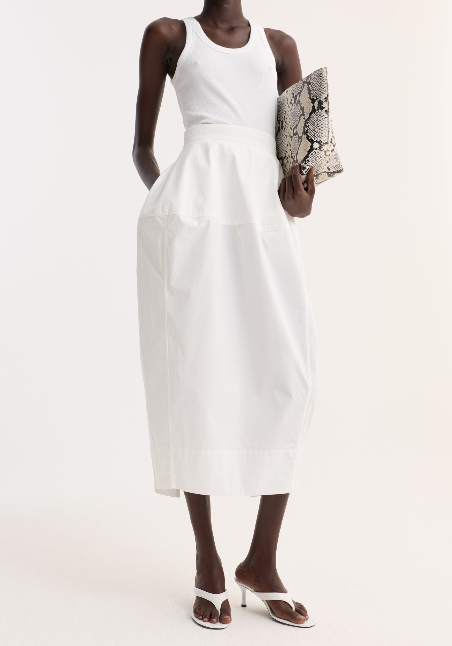 Model wearing the Sculptural poplin skirt in optic white, featuring a high waist, seam detailing, and back slit, paired with a ribbed tank top.