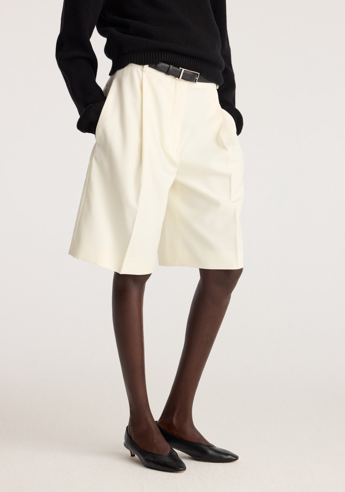 Tailored single pleat shorts | off white worn with a black sweater and belt in a studio portrait
