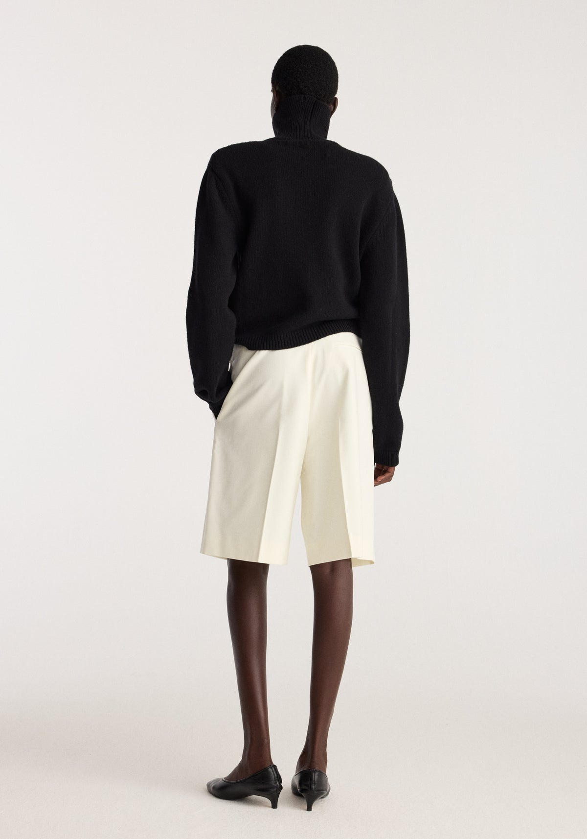 Tailored single pleat shorts | off white shown from the back on a model wearing a black sweater and black loafers in a studio setting