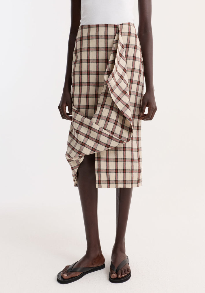 Model wearing Draped check skirt | red table check, featuring an asymmetrical front ruffle and knee-length fit, paired with a sleeveless top and sandals.