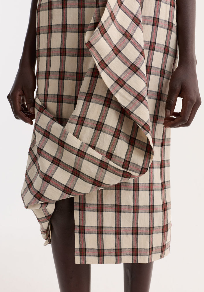 Model wearing a Draped check skirt | red table check, featuring knee-length, fitted silhouette with front ruffle drape, paired with a black crocheted hat and white tank top.