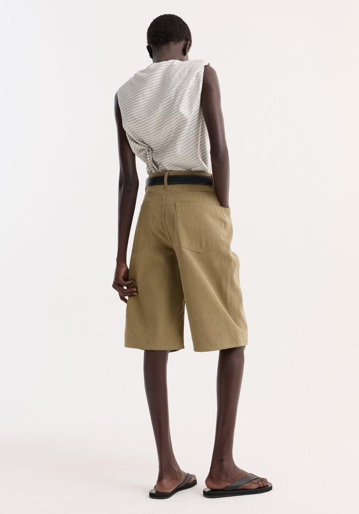 Back view of person wearing Baggy fit denim shorts | sage, featuring high-waisted, knee-length design with patch pockets, black belt, and black flip-flops.