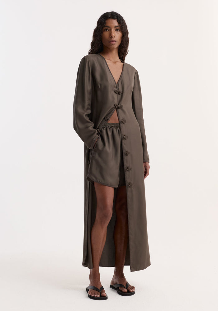 Model wears Taped silk shorts | earth with an elasticated waistband, pleated silk design, and embroidered hem, paired with a matching duster-style coat.