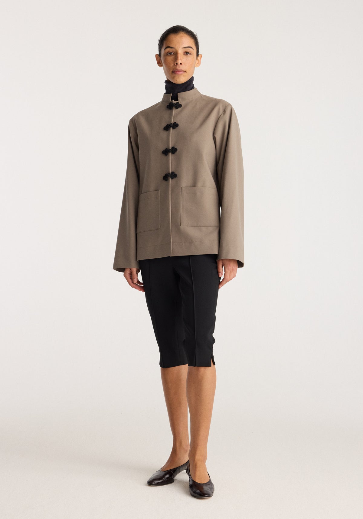 Capri | black worn as knee length black capri pants with a taupe button front jacket and black flats on a model against a neutral studio background