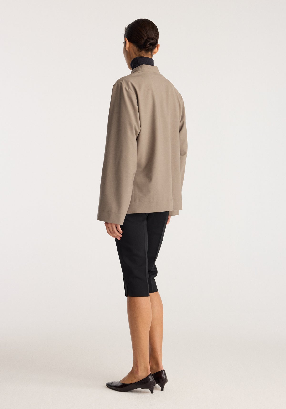 Capri | black black cropped pants shown on a model from the back with a beige jacket and black heels against a neutral studio background