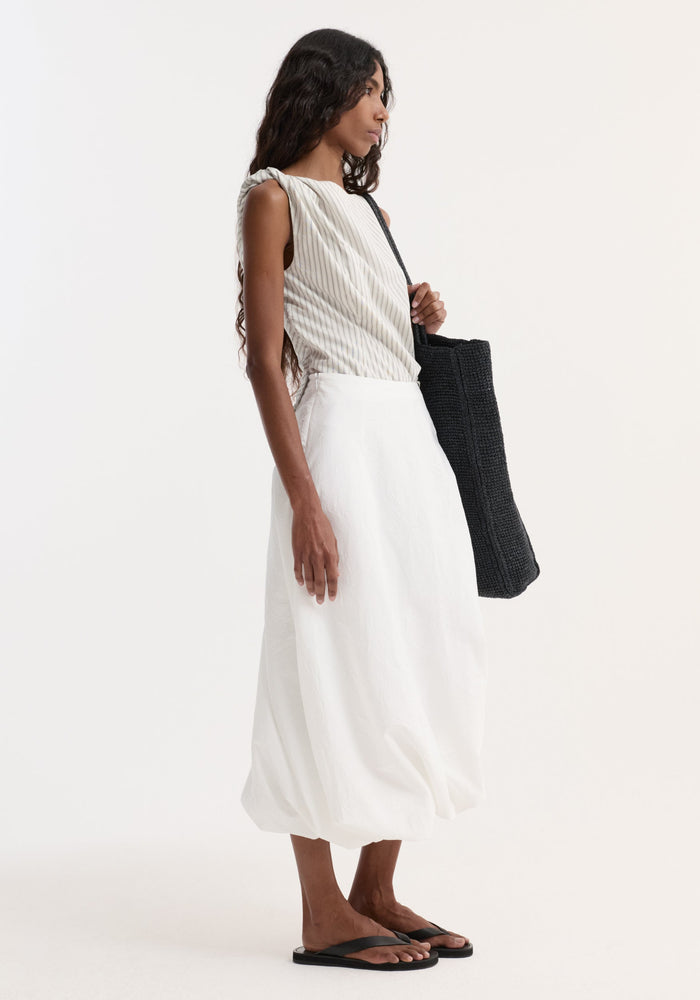 Young woman in a Twisted crushed cotton skirt, optic white, with a balloon hem and twist detail, paired with a sleeveless top and black accessories.