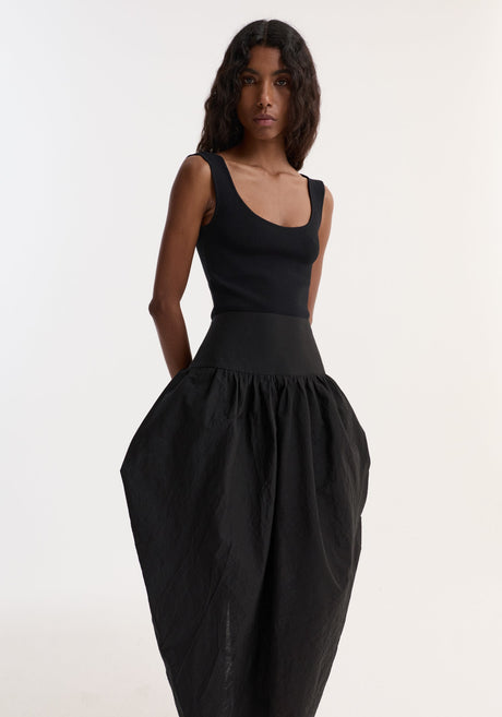 Model wearing the Sculptural volume skirt | black, featuring a mid-waist, fitted waistband, and architectural pockets, paired with a sleeveless top and strappy heeled sandals.