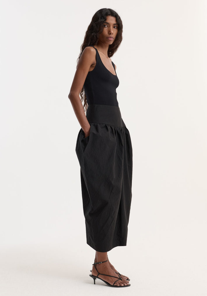 Model wearing Sculptural volume skirt | black, featuring a high-waisted, full-skirted design with architectural pockets, paired with a fitted black bodysuit and strappy sandals.