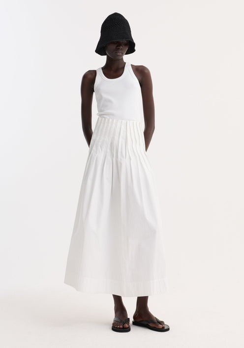 Model wearing Pleated poplin maxi skirt in optic white, featuring a high waist and flared hem, paired with a white tank and black sandals.