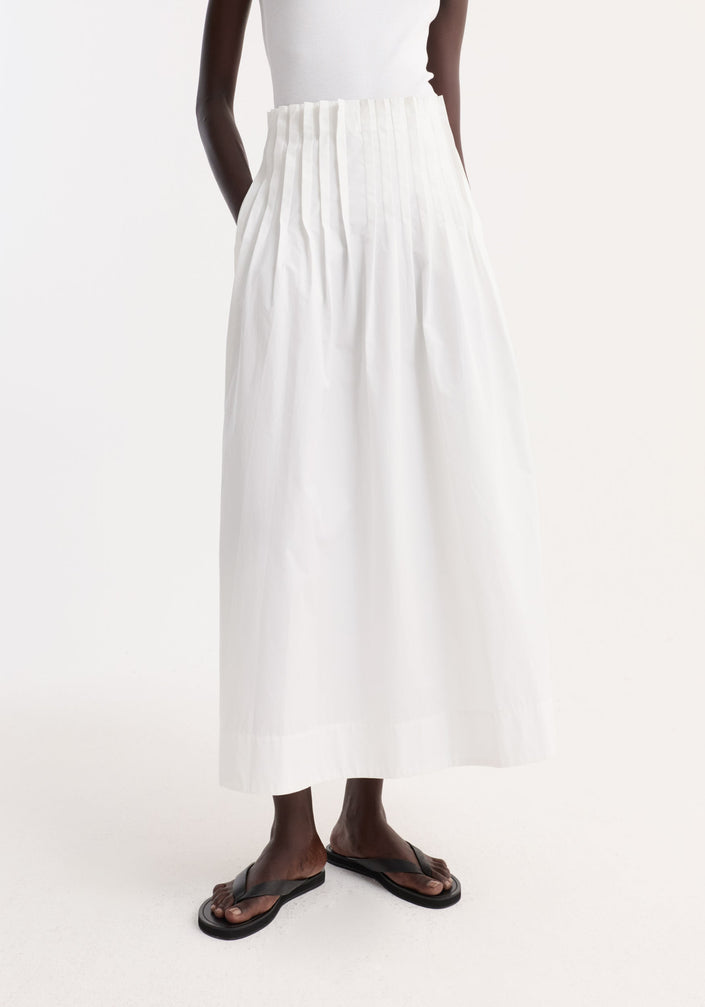 Model wearing Pleated poplin maxi skirt in optic white, featuring a high waist and flared hem, paired with a white tank and black sandals.