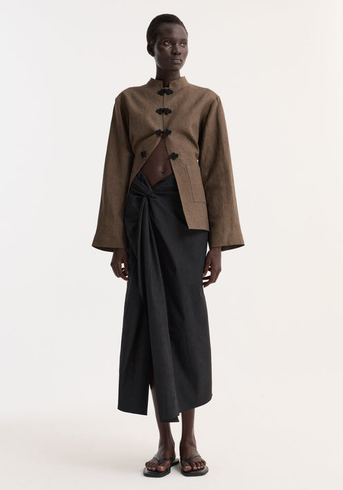 Model wearing Sarong textured skirt | black, featuring a front knot and gathered waistband. Paired with a cropped jacket, showcasing the skirt's elegant drape and style.