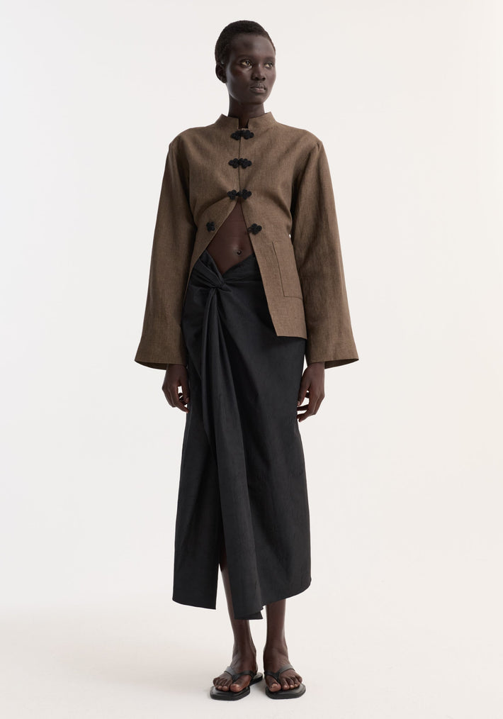 Model wearing Sarong textured skirt | black, featuring a front knot and gathered waistband. Paired with a cropped jacket, showcasing the skirt's elegant drape and style.