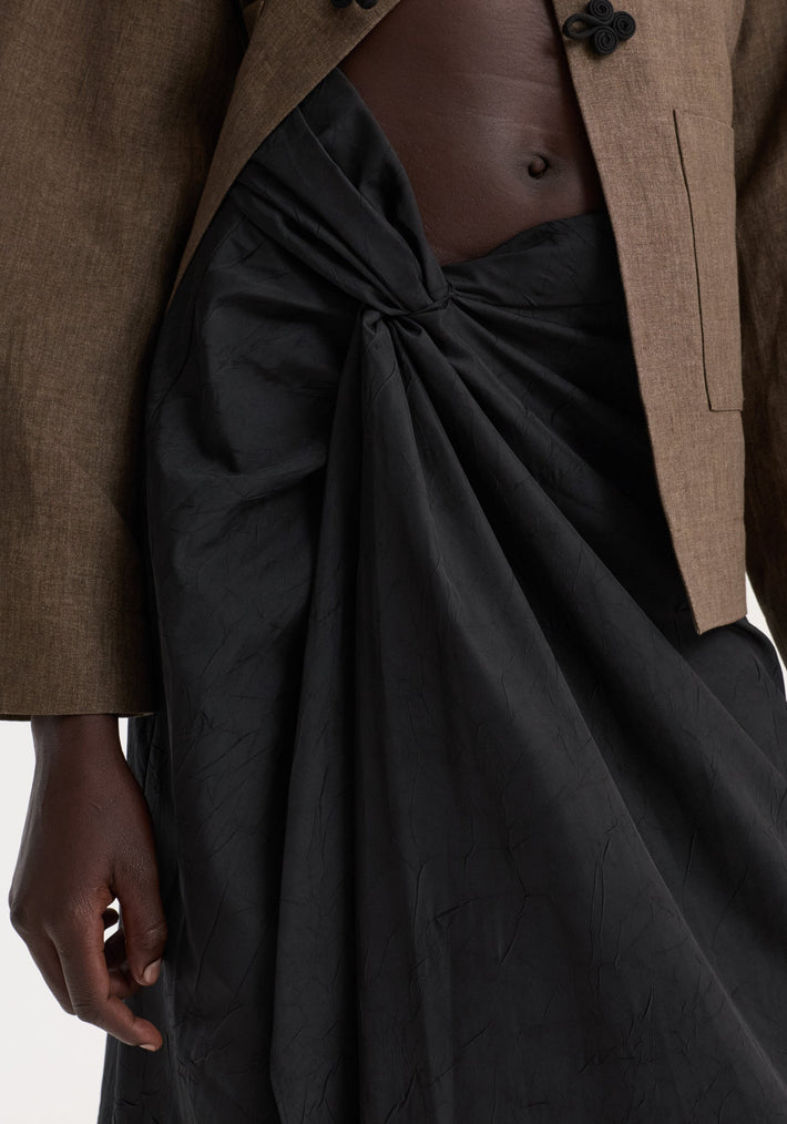 Model wearing Sarong textured skirt | black, featuring a knot detail and gathered fabric, revealing a bare midriff. Skirt offers a concealed zip for ease.