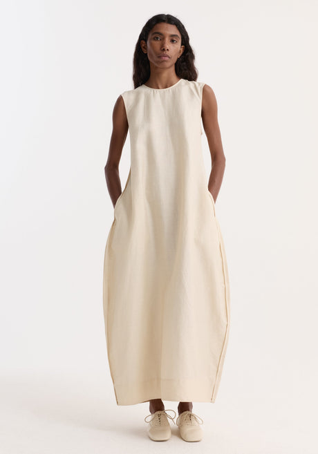 Model in Hourglass linen silk dress | butter, featuring a sleeveless, floor-length design with a sculptural silhouette and subtle side pockets, paired with cream lace-up shoes.