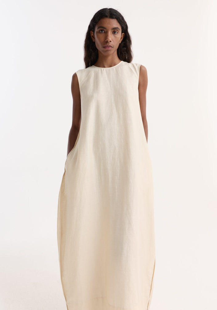Model in Hourglass linen silk dress | butter, featuring a sleeveless, floor-length design with a sculptural silhouette and subtle side pockets, paired with cream lace-up shoes.