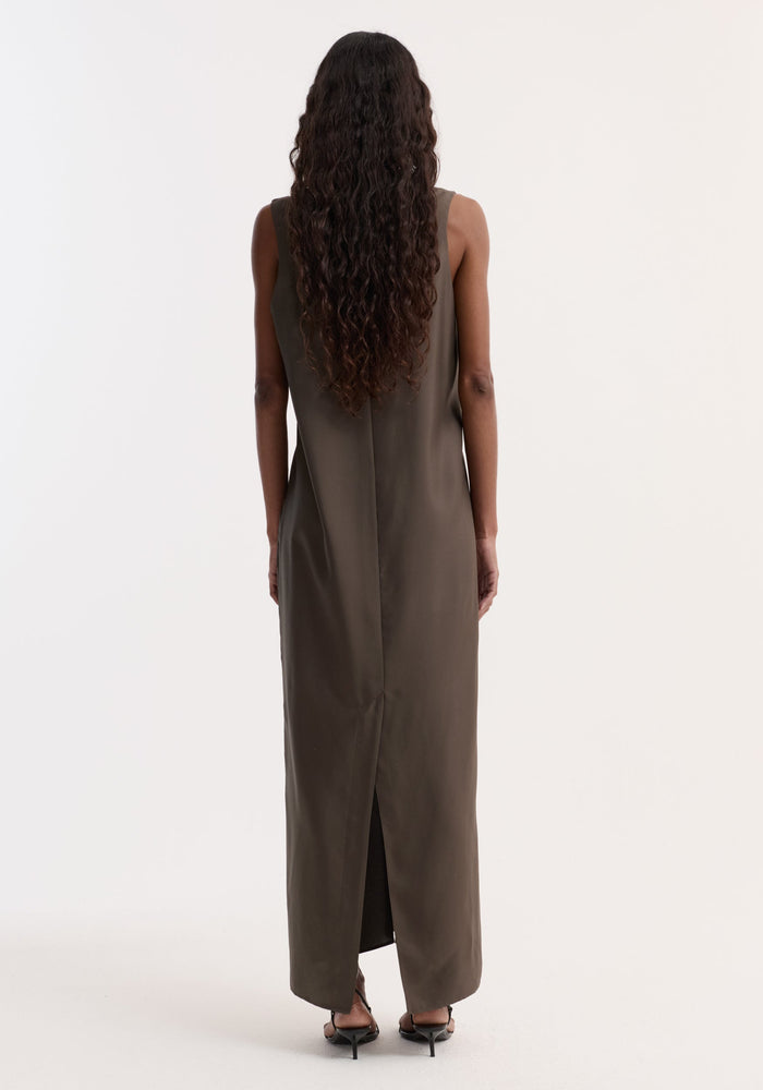 Back view of a woman in an olive-brown Silk scoop-neck dress | earth, showcasing its sleeveless, floor-length design with a slit and central back seam.